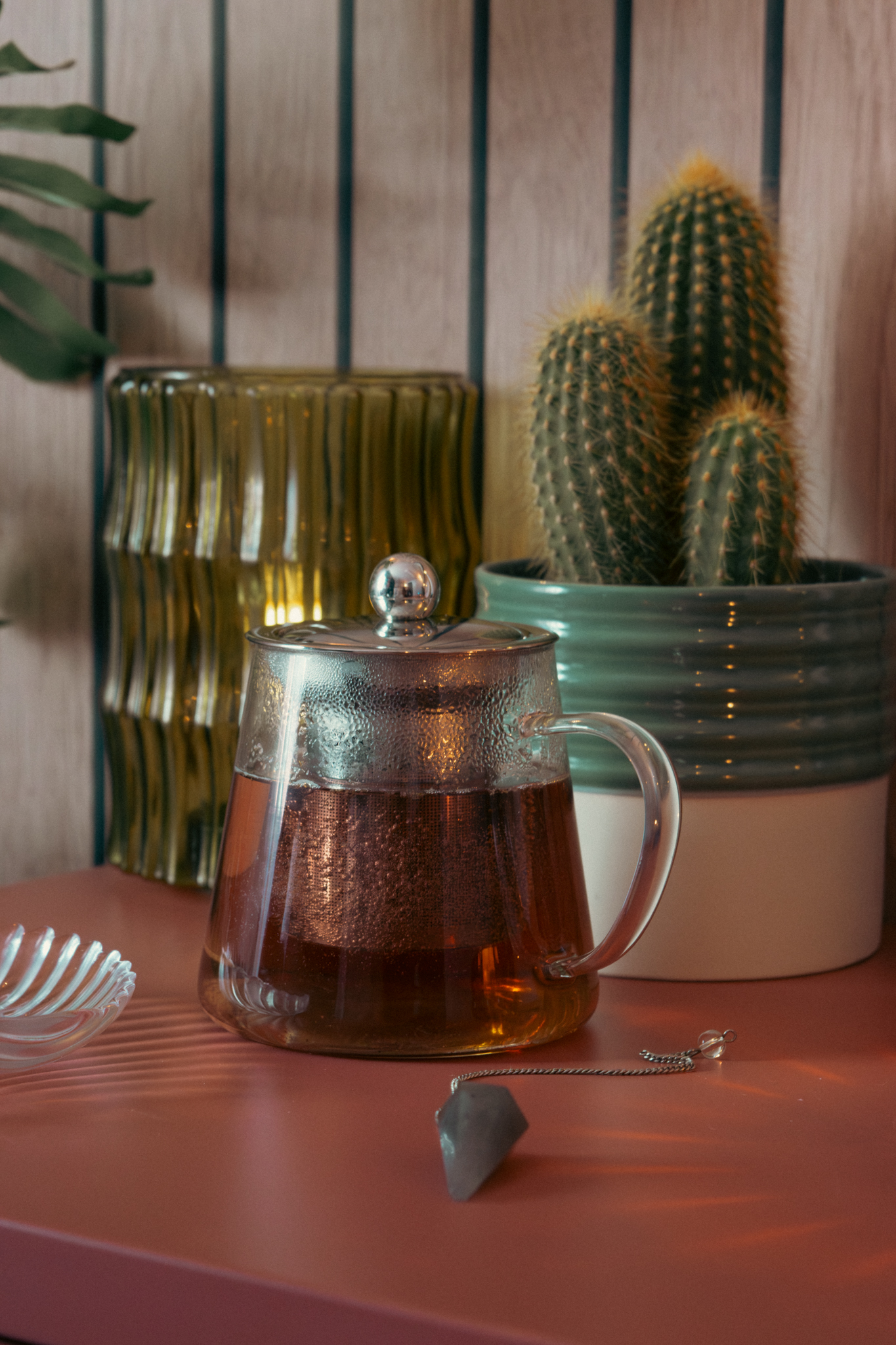 Herbal tea in a glass pot beside a cactus on the pink sideboard