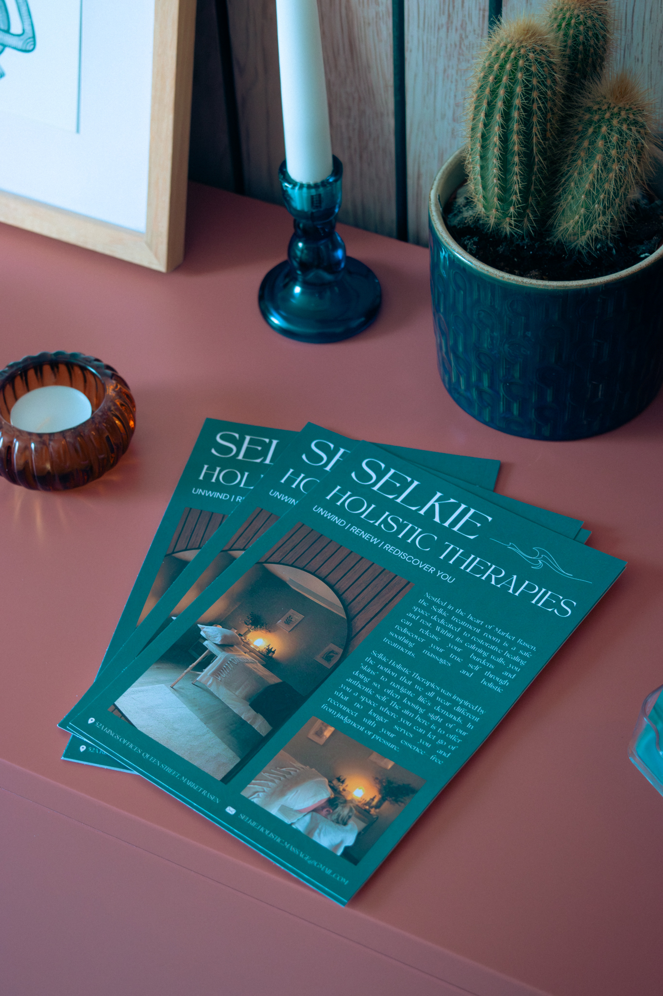 Selkie Holistic Therapies flyers on the pink sideboard beside a candle and cactus