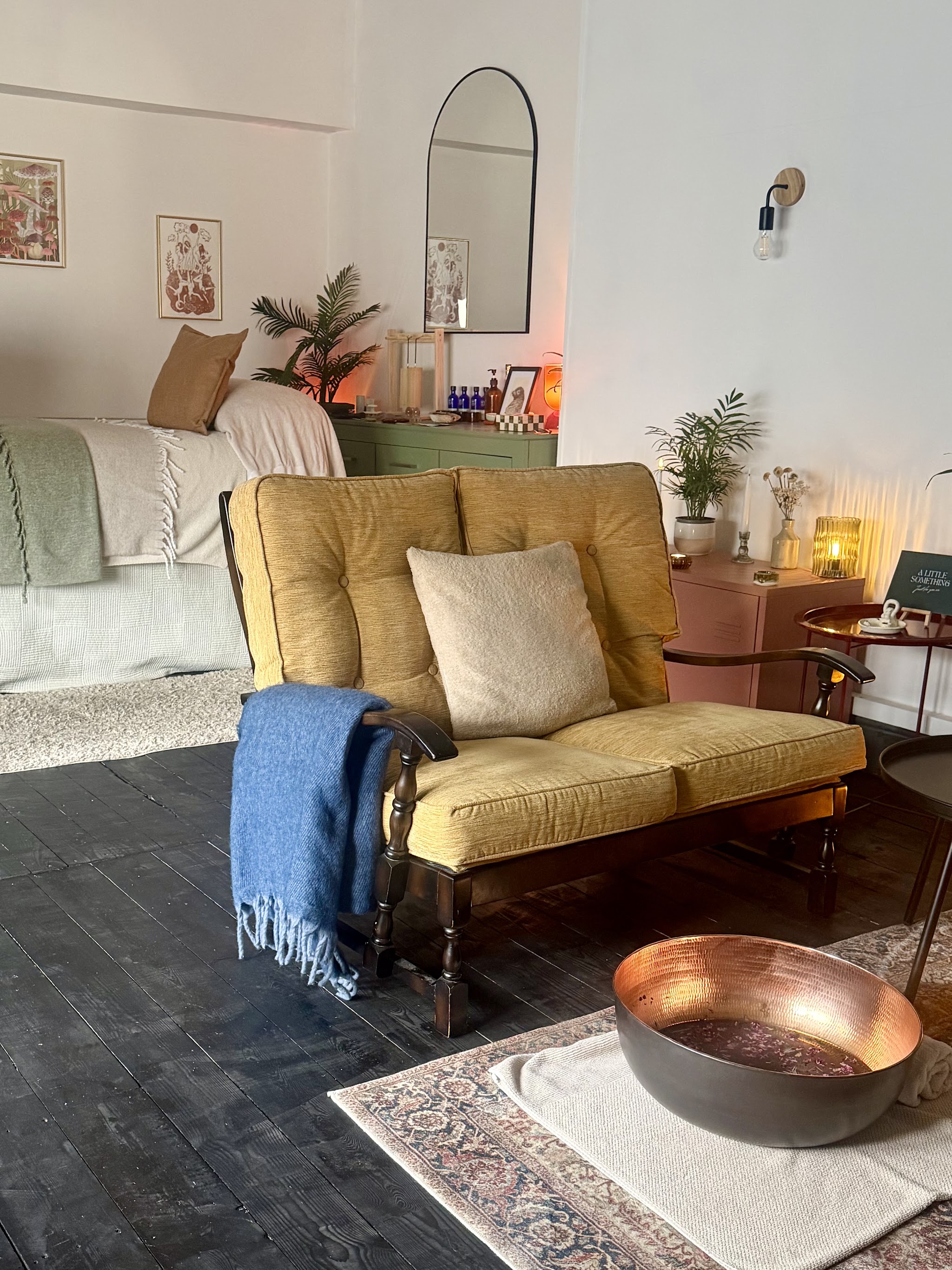 The treatment room with a yellow two-seater sofa, a blue throw and a copper foot soak bowl