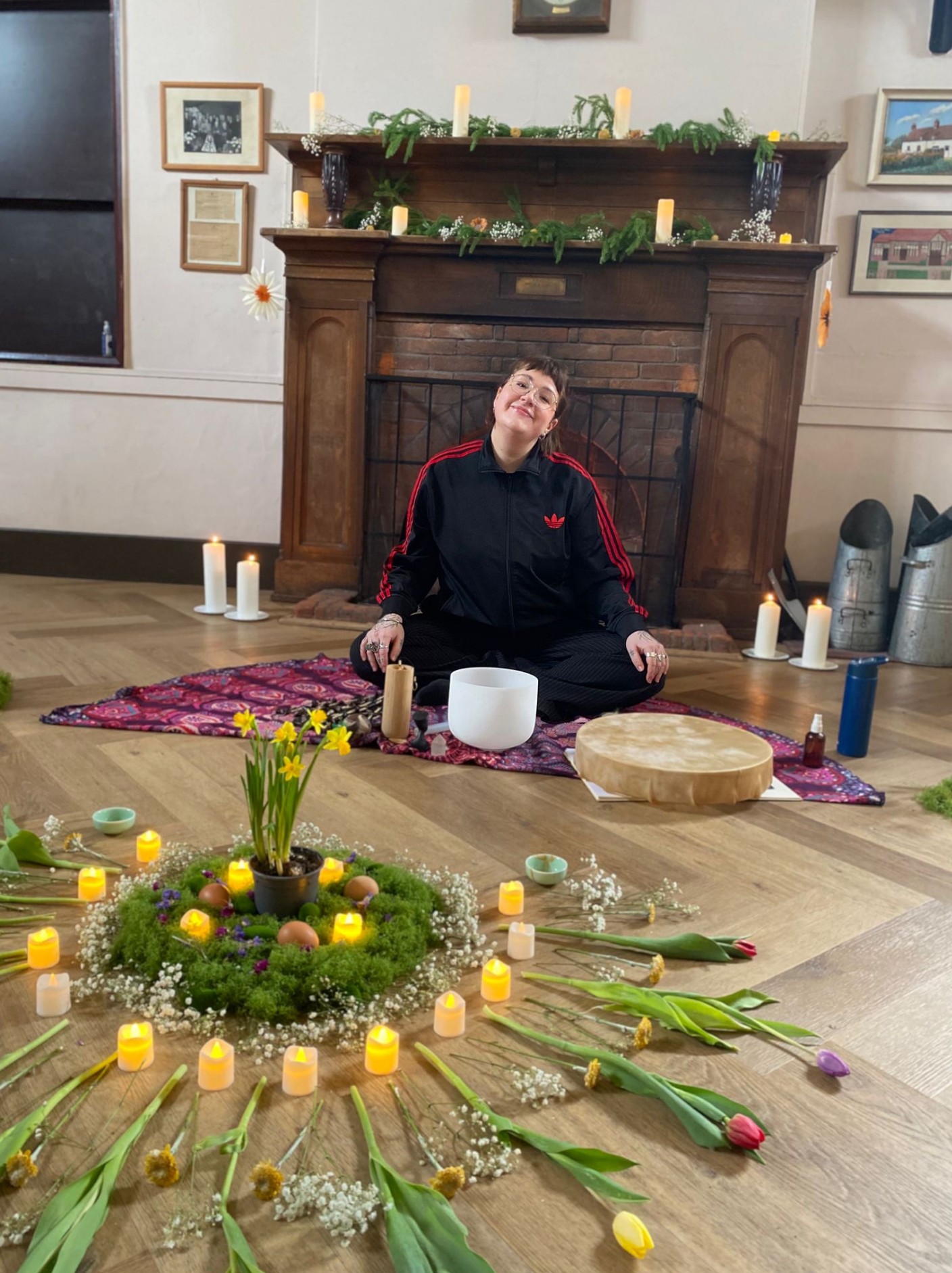 Abbi seated with a crystal bowl behind a mandala of candles, tulips and daffodils